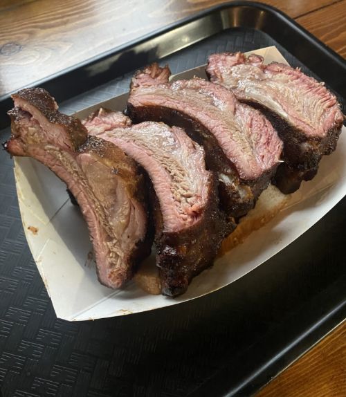 Sliced smoked pork ribs showing pink smoke ring and charred bark on a paper-lined black tray.