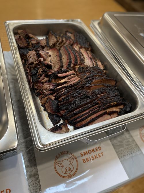 Sliced smoked brisket with charred bark in a metal chafing pan on a buffet labeled smoked brisket.
